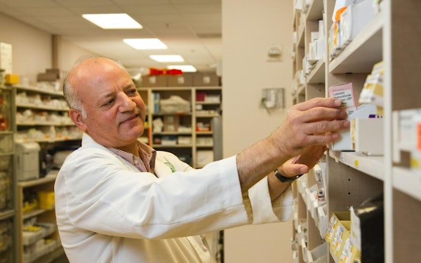 A pharmacist reaches for medication on a high shelf.