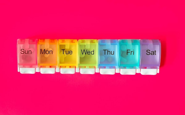 A weekly pill organizer against a red background.
