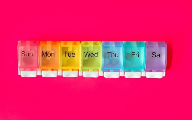 A weekly pill organizer against a red background.