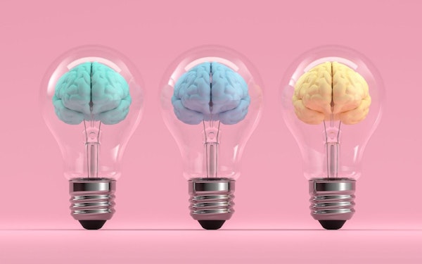 Three pastel colored brains inside three light bulbs against a pink background.