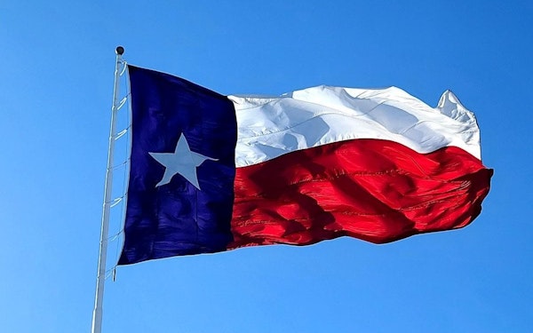 The Texas state flag blowing in the window against the blue sky.