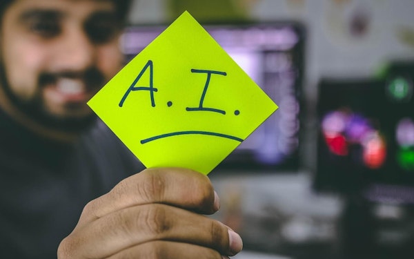 A man holds up a green sticky note that has the text "A.I." written on it.