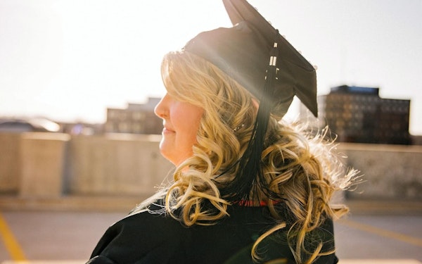 A woman stands outside wearing a black graduation gown and robe.