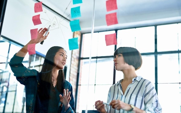 Two students in a conference room plan a project using post-it notes.