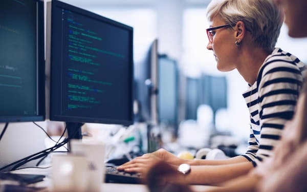 A person sits at a desk in front of a computer displaying lines of code.