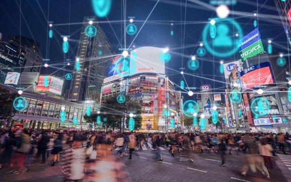 People walking around in a city with an overview of a graphic design showing a web of silhouetted blue icons.