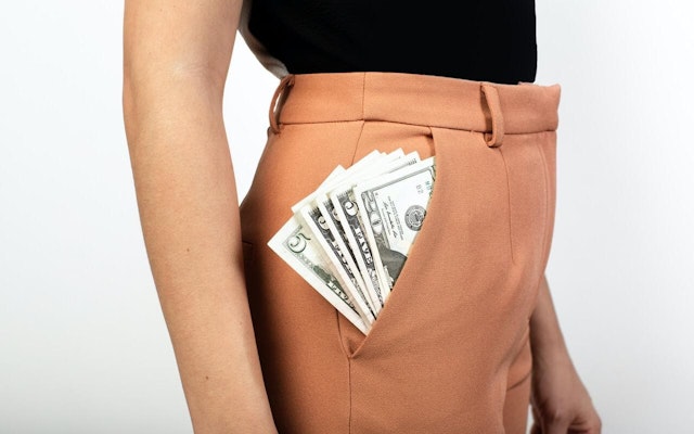 A person with lots of printed currency sticking out of their pocket.