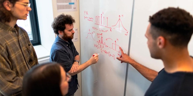 Graduate students reviewing diagrams on a whiteboard