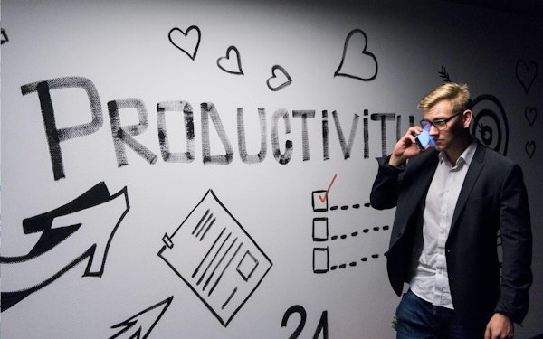 A person speaking on their smartphone while walking past wall art that reads "Productivity."