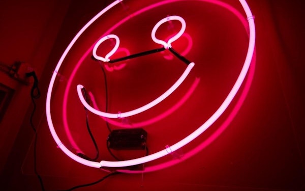 A pink neon smiley face light glows in a dark room.