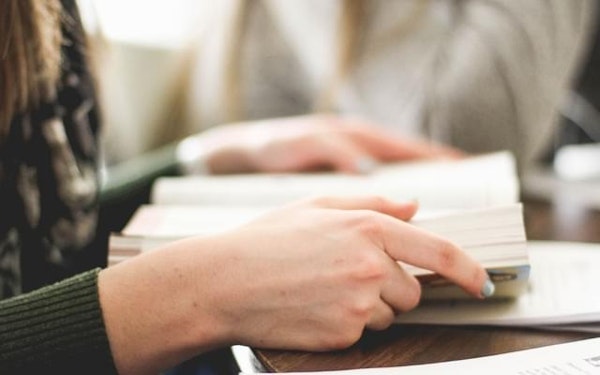 A student holds open a book on a brown table.