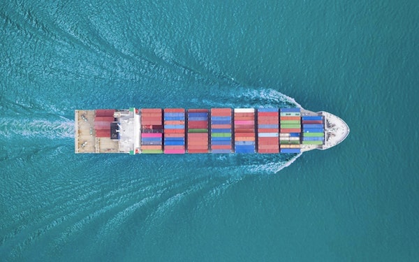 An aerial view of a colorful, loaded cargo ship moving across the ocean.