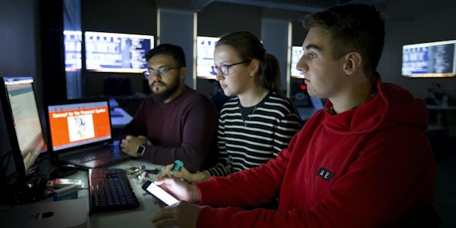 Three Stevens students working together at a desktop in the computer lab.