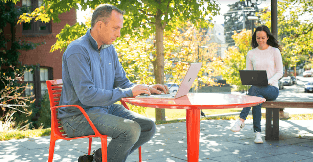 Students work on their laptops in an outdoor seating area.