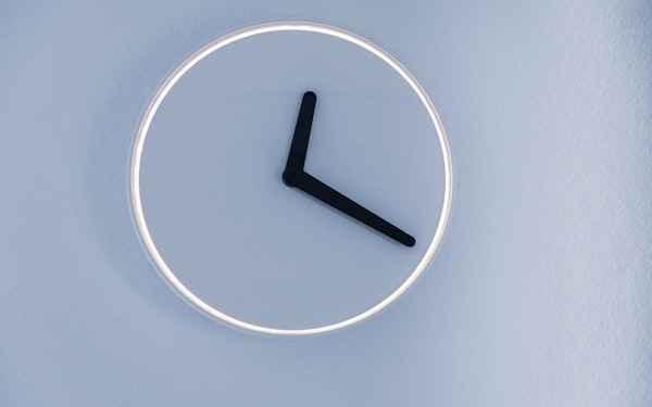 A minimalist neon sign wall clock on a light blue background.